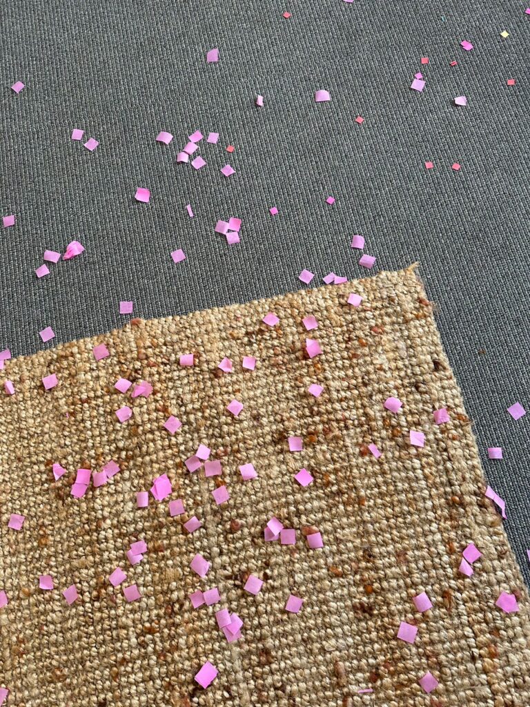 Rosafarbene quadratische Konfettis liegen auf dem Teppichboden.