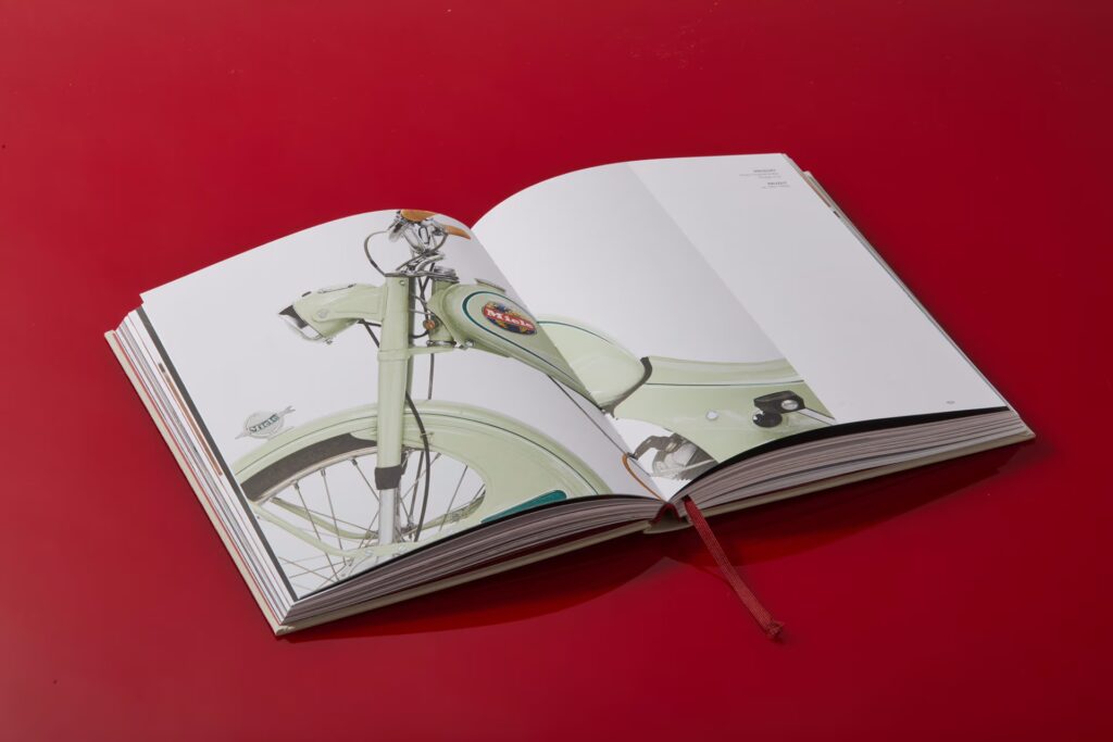 Das Miele-Buch liegt aufgeklappt auf rotem Hintergrund. Zu sehen ist eine Doppelseite mit dem Foto des hellgrünen Moped-Rollers.