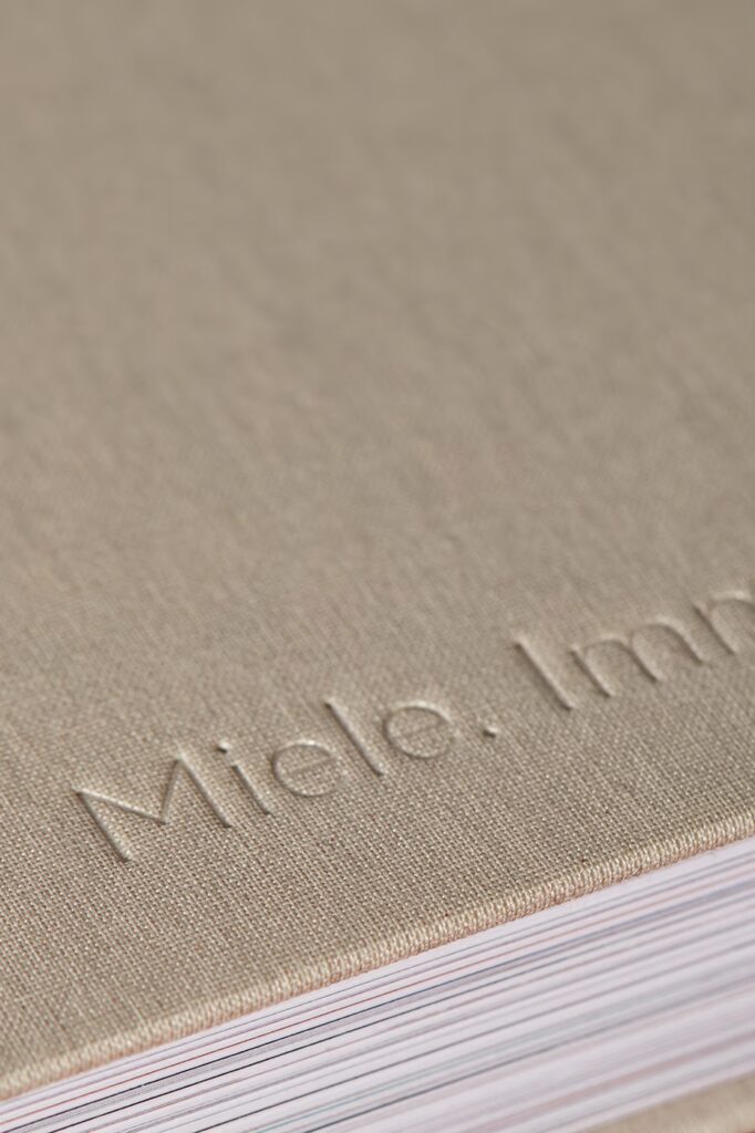 Nahaufnahme der Buch-Rückseite. Beige-farbiger Stoffeinband mit dem Wort Miele eingeprägt.
