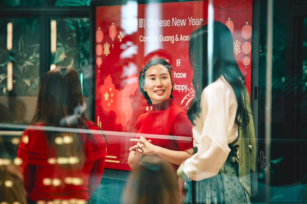Drei Asiatinnen sind im Gespräch. Im Hintergrund ist ein rotes Plakat mit der Aufschrift "Chinese New Year" zu sehen.