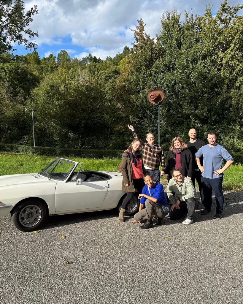 Mehrere Personen von birke und partner stehen mit Mitarbeitern der Firma Stihl draußen vor einem weißen Oldtimer und winken in die Kamera.