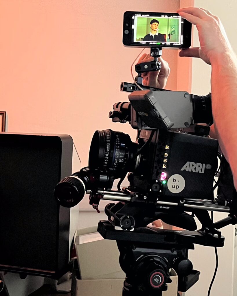 Eine professionelle Filmkamera. Darüber hält eine Hand ein Smartphone. Auf dem Display ist ein junger Mitarbeiter von STIHL zu sehen.