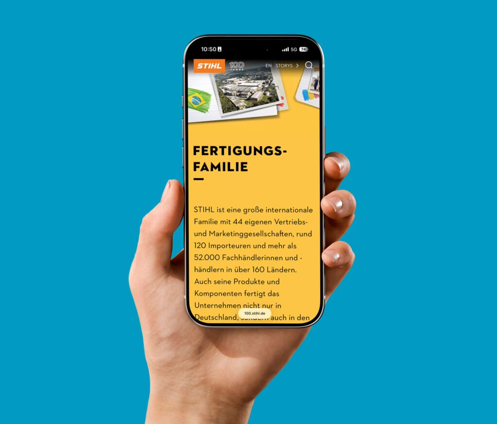 Eine Hand hält ein Smartphone mit gelbem Display zur Kamera, auf dem eine STIHL-Story mit dem Titel Fertigungsfamilie zu sehen ist. Der Hintergrund ist blau.