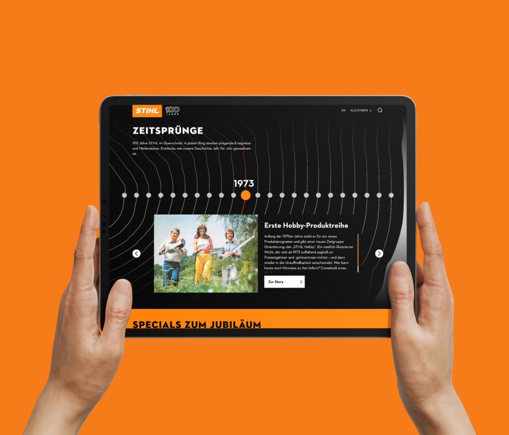 Zwei Hände halten das Display eines Tablets zur Kamera. Gezeigt wird eine STIHL-Webseite mit dem Titel Zeitsprünge. Der Hintergrund ist orange.