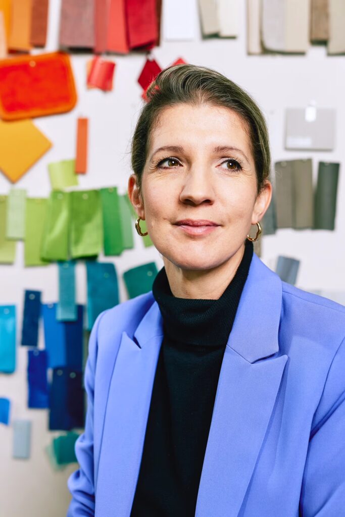 Porträtfoto der Produktdesignerin Lisa Werner vor einer Wand mit Stoffmustern in unterschiedlichen Farben.