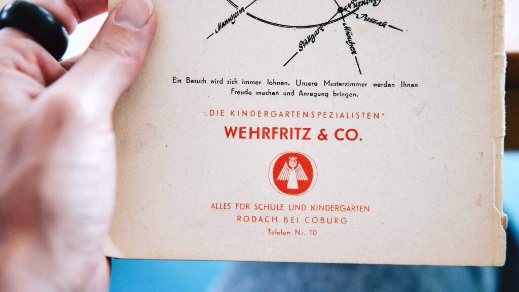 Eine Hand hält eine alte Katalog-Rückseite, auf der ein früheres Wehrfritz-Logo zu sehen ist.