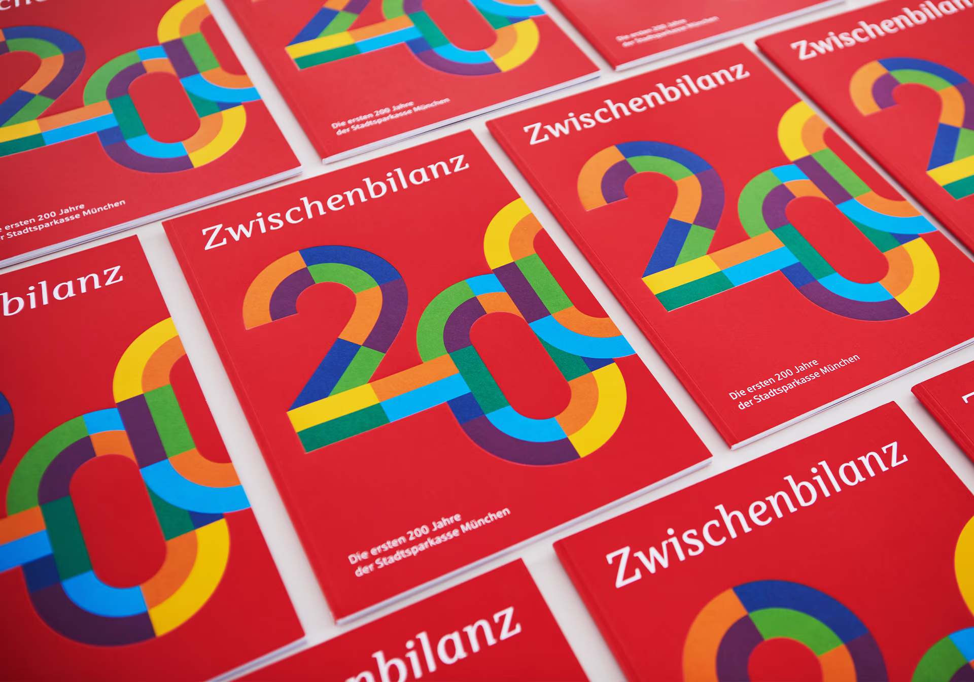 Mehrere Magazincover liegen in mehreren Reihen auf einer Fläche. Das Cover zeigt eine 200, den Titel Zwischenbilanz und den Untertitel: Die ersten 200 Jahre der Stadtsparkasse München.