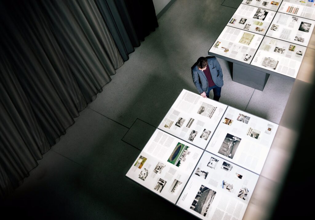 Draufsicht auf Tische mit Ausstellungsinhalten aus dem NS-Dokumentationszentrum, die von einem Mann angesehen werden.